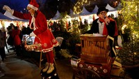 Seorang wanita berpakaian seperti Sinterklas dan seorang musisi tampil di depan kios-kios pasar Natal Notre-Dame di Paris. REUTERS/Stephanie Lecocq