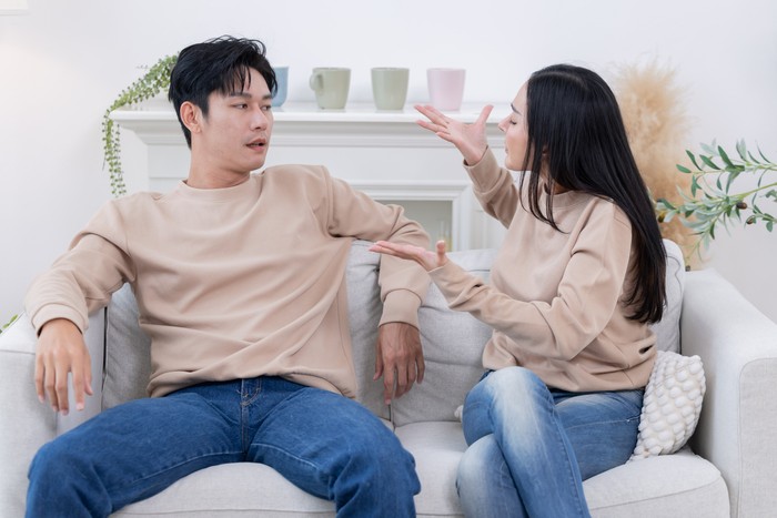 A couple sits on a couch having a fight, displaying clear signs of tension and disagreement