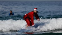 Seorang peselancar berkostum Sinterklas menjaga keseimbangan di atas papan, memadukan olahraga ekstrem dengan nuansa liburan akhir tahun. REUTERS/Ammar Awad