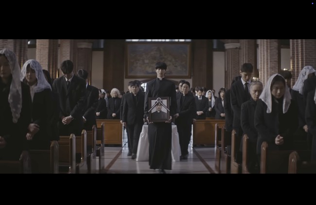 Kemudian terungkap bahwa Byeon Woo Seok memimpin prosesi pemakaman. Ia membawa potret kenangan aktor Park Hee Seon, yang juga diperlihatkan sebagai pastor di awal video. Foto: dok. YouTube @DolphinersOfficial