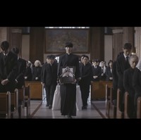 Kemudian terungkap bahwa Byeon Woo Seok memimpin prosesi pemakaman. Ia membawa potret kenangan aktor Park Hee Seon, yang juga diperlihatkan sebagai pastor di awal video. Foto: dok. YouTube @DolphinersOfficial