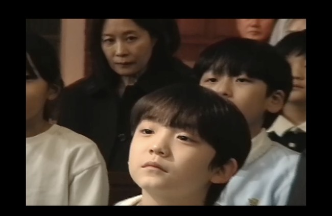 Di akhir video, aktris Moon So Ri muncul sebagai wanita misterius, mengawasi bocah yang menahan jari Byeon Woo Seok. Lewat project The Christmas Song, sutradara Shin Woo Seok kembali menuai pujian dengan visual dan narasinya. Ialah yang menggarap video klip Ditto, OMG, dan Cool With You dari NewJeans. Foto: dok. YouTube @DolphinersOfficial