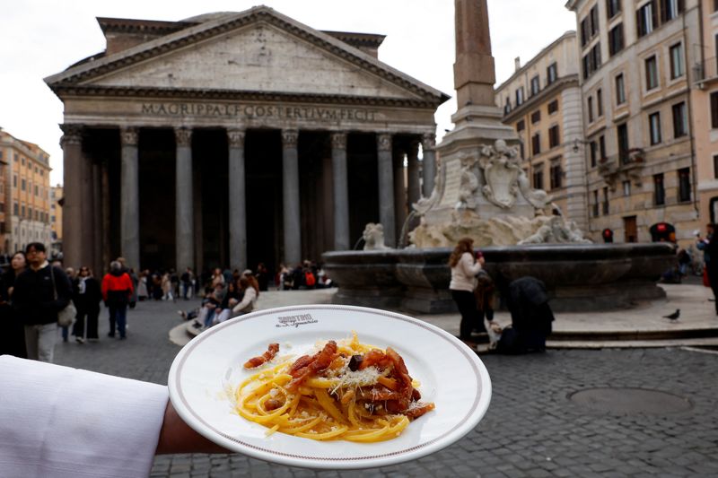 A waiter shows a plate of traditional pasta Carbonara in front of the Pantheon as Italian cuisine awaits a crucial UNESCO decision that could recognise it as an Intangible Cultural Heritage of Humanity in this illustration picture taken in Rome, Italy, December 3, 2025. REUTERS/Remo Casilli/ Illustration