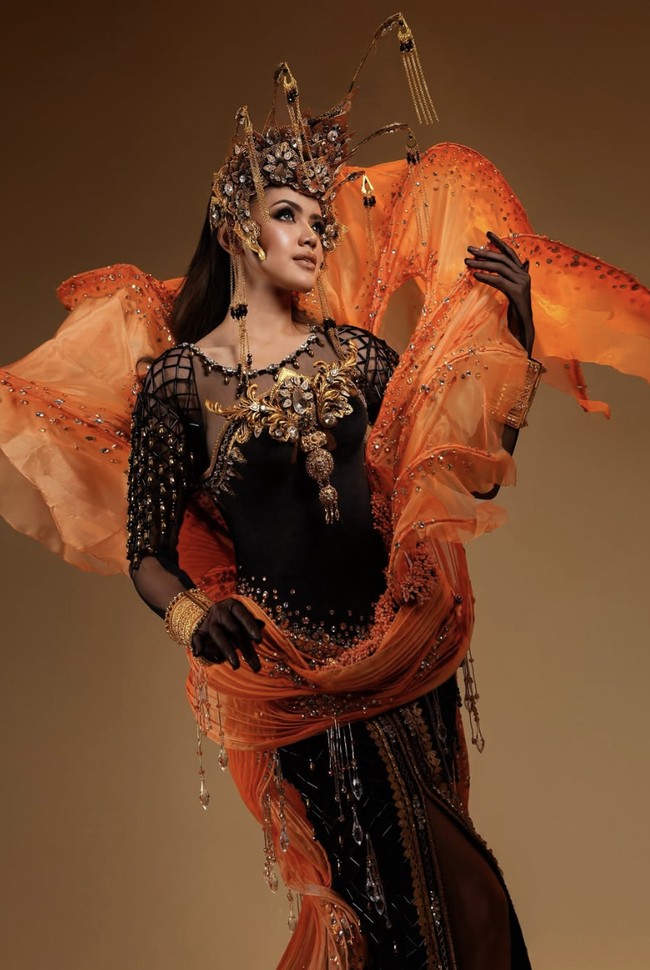 Busana yang ia kenakan merupakan dress berpotongan kebaya berwarna hitam yang dipadukan dengan lapisan oranye transparan menyerupai tentakel ubur-ubur. Sentuhan ini membuat siluetnya terlihat semakin hidup, seolah bergerak mengikuti langkahnya. Foto: dok. Instagram @rinandamh