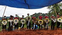 Petugas polisi membawa karangan bunga untuk diletakkan di makam korban tak dikenal dari banjir bandang dan tanah longsor. Para pejabat pemerintah daerah di Sumatera telah meminta pemerintah pusat di Jakarta untuk menyatakan keadaan darurat nasional guna membebaskan dana tambahan untuk upaya penyelamatan dan bantuan. Foto: REUTERS/Willy Kurniawan
