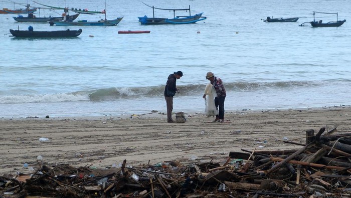 Seorang nelayan berjalan di dekat tumpukan sampah dampak cuaca ekstrem di kawasan Pantai Kelan, Badung, Bali, Kamis (11/12/2025). Menurut nelayan setempat, sampah kiriman berupa kayu, bambu, dan plastik yang berserakan di pesisir pantai tersebut mulai terjadi sejak awal bulan Desember akibat terbawa gelombang tinggi disertai angin kencang. ANTARA FOTO/Nyoman Hendra Wibowo