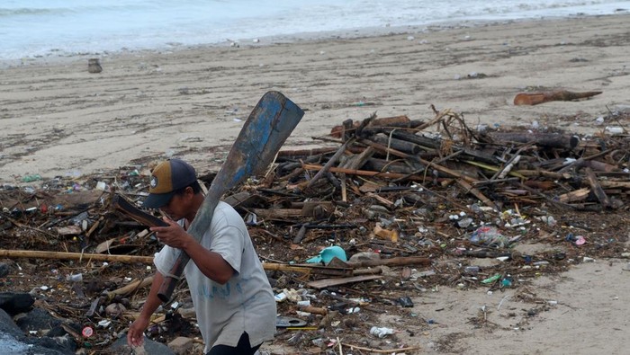 Seorang nelayan berjalan di dekat tumpukan sampah dampak cuaca ekstrem di kawasan Pantai Kelan, Badung, Bali, Kamis (11/12/2025). Menurut nelayan setempat, sampah kiriman berupa kayu, bambu, dan plastik yang berserakan di pesisir pantai tersebut mulai terjadi sejak awal bulan Desember akibat terbawa gelombang tinggi disertai angin kencang. ANTARA FOTO/Nyoman Hendra Wibowo