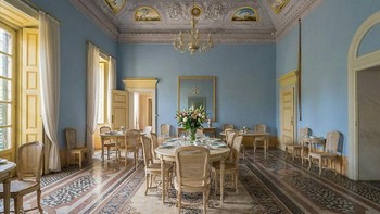 Ruang Makan yang Kusam Jadi Elegan. Before: Ruang makan bergaya klasik tampak kusam, berdebu, dan dipenuhi kursi rusak yang menumpuk di tengah ruangan. After: AI memperlihatkan tampilan lamanya—ruang makan cerah dengan dinding biru bersih, chandelier, meja makan lengkap, dan tata letak elegan seperti ruang bangsawan. Foto: Boredpanda