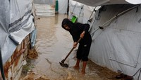 Seorang anak berusaha menggali parit darurat untuk mengalirkan air hujan yang membanjiri lorong-lorong antar tenda. Hujan musim dingin yang terus turun membuat banyak tenda terendam, meningkatkan risiko penyakit terutama bagi anak-anak dan lansia. REUTERS/Mahmoud Issa