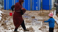 Seorang ibu dan anaknya mencoba menjauhi area licin di dekat tempat mandi portabel yang terendam air. UNRWA memperingatkan bahwa kurangnya perlindungan cuaca dan keterbatasan bantuan membuat puluhan ribu pengungsi rentan terhadap hipotermia dan infeksi selama musim dingin ini. REUTERS/Mahmoud Issa