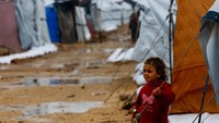 Seorang anak berdiri di antara tenda dan jalan berlumpur. UNRWA menekankan bahwa bantuan ke Gaza masih jauh dari cukup, dan perlindungan terhadap cuaca buruk harus segera ditingkatkan untuk mencegah lebih banyak korban. REUTERS/Mahmoud Issa
