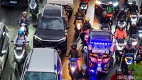 Pengendara sepeda motor berhimpitan di antara mobil, mencari celah agar bisa melaju di tengah kemacetan panjang. 