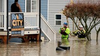 Petugas penyelamat berjalan di depan rumah yang terendam banjir, menggambarkan banjir besar akibat sungai-sungai utama seperti Snohomish yang meluap. Hujan dari atmospheric river diperkirakan menumpahkan hampir 5 triliun galon air ke wilayah Washington. REUTERS/David Ryder