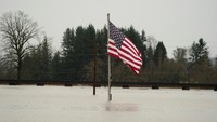 Sebuah bendera AS berdiri di tengah genangan luas, mencerminkan skala banjir yang menenggelamkan seluruh lingkungan. Wilayah Washington dan Oregon mencatat salah satu banjir paling merusak dalam dekade terakhir. REUTERS/David Ryder