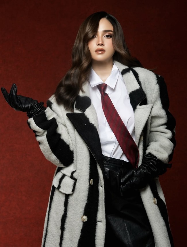 Syifa memadukan mantel tersebut dengan kemeja putih clean dan dasi merah burgundy bermotif garis, memberikan sentuhan maskulin. Untuk bawahannya ia tampak mengenakan celana kulit bertekstur warna hitam. Foto: Instagram/@syifahadju