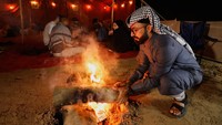 Beberapa duduk mengelilingi api unggun, sementara yang lain menyaksikan matahari terbenam dengan latar langit yang memerah keemasan. REUTERS/Alaa Al-Marjani