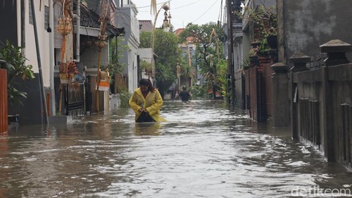 Seorang warga di Perumahan Widuri Permai Jalan Gunung Athena, Denpasar, menerobos genangan banjir, Minggu (14/12/2025). (Foto: Aryo Mahendro/detikBali)
