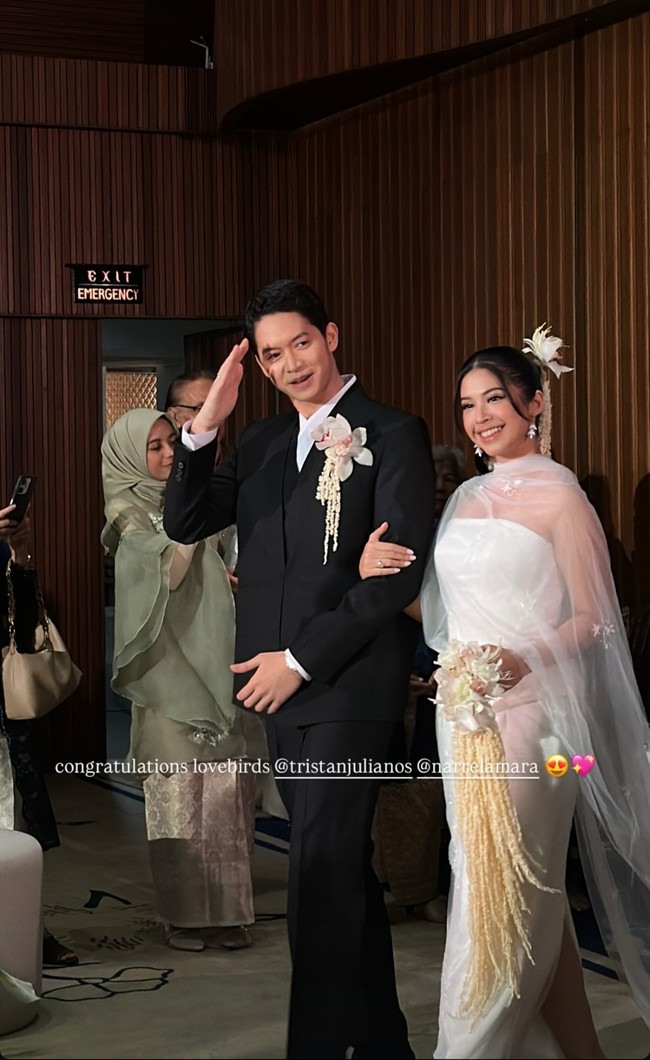 Pada acara resepsi, pasangan pengantin ini berganti kostum yang tak kalau memukau. Tristan Juliano mengenakan tuxedo hitam dipadu kemeja putih dan aksen bunga di dada, sementara Narrel Amara tampil chic dalam gaun putih dengan outer sheer serta hiasan bunga di kepala. Foto: dok Instagram fanisawidya