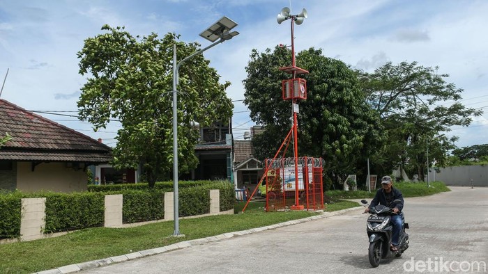 Pengendara melintas di depan mesin Early Warning System (EWS) banjir di Bekasi, Senin (15/12/2025). Dipasangnya early warning system (EWS) banjir di sejumlah titik rawan ini untuk memperkuat mitigasi bencana saat musim hujan. Perangkat peringatan dini ini tersebar di wilayah yang berada di sepanjang aliran sungai dan kawasan permukiman yang kerap terdampak luapan air, khususnya di Daerah Aliran Sungai (DAS) Kali Bekasi dan sekitarnya.