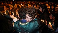 Para pelayat memeluk satu sama lain sambil menyalakan lilin dalam doa bersama untuk para siswa yang meninggal akibat kecelakaan bus, di luar Liceo Antioqueño, Bello, Kolombia, Minggu (14/12/2025). REUTERS/Juan David Duque