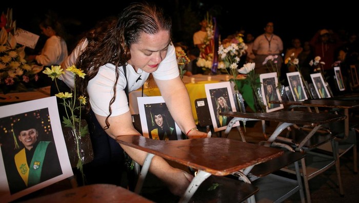 A woman arranges school desks displaying photographs of students during a vigil for victims of a bus accident, outside the Liceo Antioqueno in Bello, Colombia, December 14, 2025. REUTERS/Juan David Duque