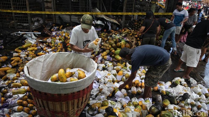 Para pedagang menyortir pepaya yang masih bisa diselamatkan usai kebakaran melanda los buah di Pasar Induk Kramat Jati, Jakarta Timur, Senin (15/12/2025).