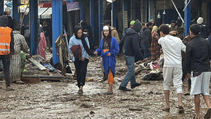 SAFI, MOROCCO - DECEMBER 15: People are trying to walk down the mud covered street as teams continue their work across the city to repair and clean up the damage caused by the flood in the mud covered streets of the Safi, Morocco on December 15, 2025. The death toll from flash floods in the western city of Safi rose to 21, Moroccan authorities announced. Search and rescue operations are ongoing, and necessary measures have been taken to secure the affected areas and provide support to residents, it added. (Photo by Stringer/Anadolu via Getty Images)