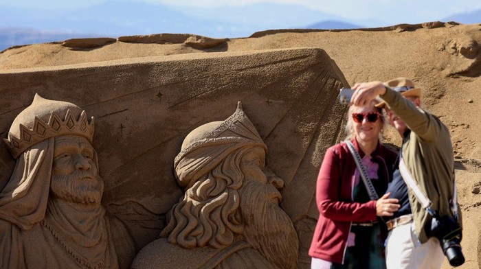 Two tourists take a photo next to a sand sculpture representing a Christian nativity scene on Las Canteras beach in Las Palmas de Gran Canaria, Spain, December 15, 2025. REUTERS/Borja Suarez