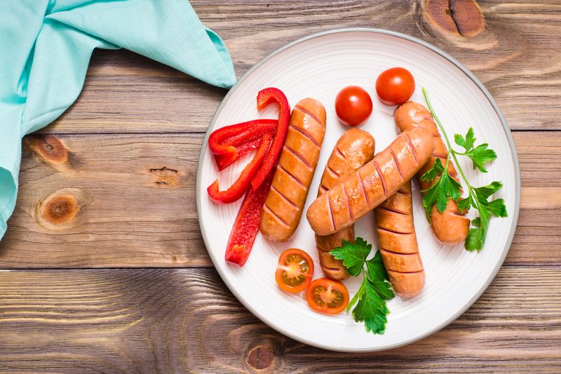 Grilled sausages, fresh tomatoes, peppers and parsley on a plate on a wooden table. Top view