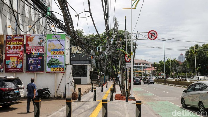 Kabel utilitas tampak semrawut dan menjuntai hingga ke trotoar di Jalan Prof Dr Soepomo, Tebet, Jakarta, Selasa (16/12/2025). Kondisi ini menutup jalur pejalan kaki.