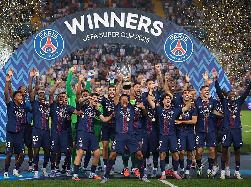 UDINE, ITALY - AUGUST 13: Marquinhos of PSG lifts the trophy as he celebrates with team mates Lucas Chevalier, Achraf Hakimi, Marquinhos, Khvicha Kvaratskhelia, Ousmane Dembele, Desire Doue, Vitinha, Nuno Mendes, Bradley Barcola, Warren Zaire-Emery, Willian Pacho, Matvei Safonov, Renato Martin, Lucas Beraldo, Fabian Ruiz, Goncalo Ramos, Kang-in Lee, Lucas Hernandez, Noham Kamara, Ibrahim Mbaye and Illia Zabarnyi and Head Coach Luis Enrique following the penalty shoot out victory in the UEFA Super Cup 2025 match between Paris Saint-Germain and Tottenham Hotspur at Friuli Stadium on August 13, 2025 in Udine, Italy. (Photo by Jonathan Moscrop/Getty Images)