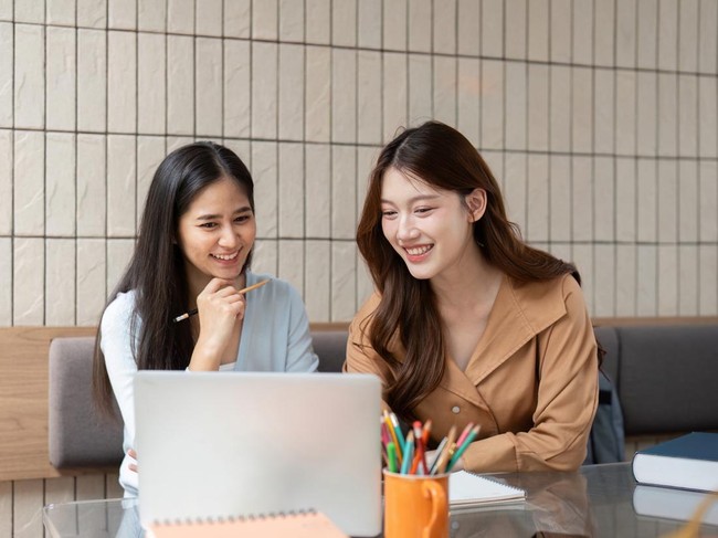Amused expressions as both friends celebrate a breakthrough while working on a project together in a bright atmosphere.