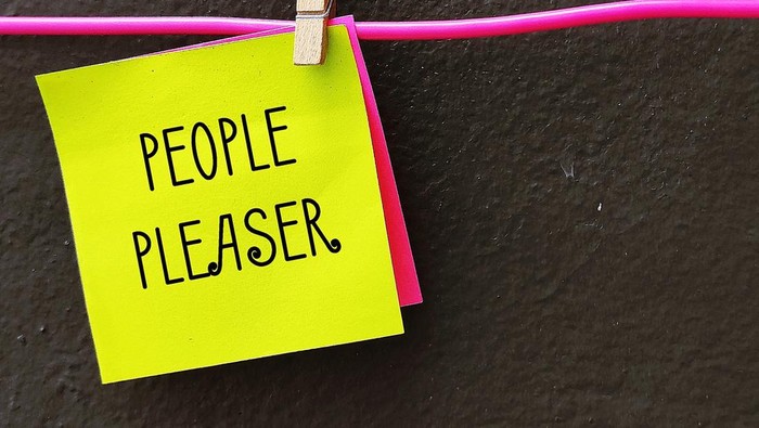 Yellow note clipped with hanger wire with handwritten PEOPLE PLEASER, concept of one who tries hard to make others happy even go out of their way, time or resources,overly concerned with pleasing others