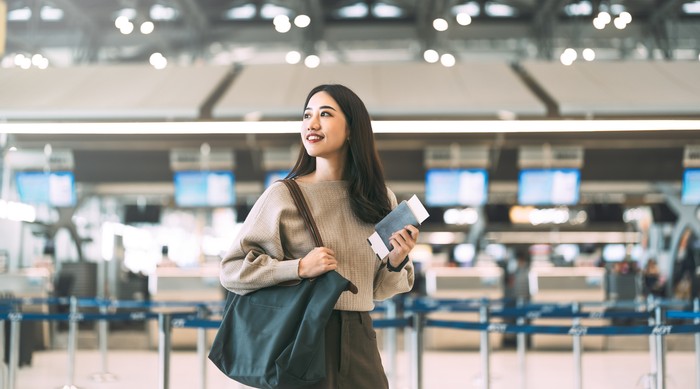 Passenger at international airport terminal for departure with airline transport. Portrait of standing tourist woman holding passport and boarding pass to transit.
