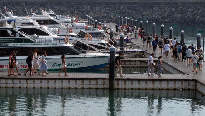 Wisatawan berjalan di dermaga apung saat akan menyeberang ke Pulau Nusa Penida menggunakan kapal cepat di Pelabuhan Sanur, Denpasar, Bali, Jumat (19/12/2025). Kantor Kesyahbandaran dan Otoritas Pelabuhan (KSOP) Kelas II Benoa, Bali, memastikan kelaikan 67 kapal cepat atau boat di Pelabuhan Sanur dan Serangan Denpasar untuk melayani peningkatan penumpang pariwisata jelang libur Natal dan Tahun Baru 2026. ANTARA FOTO/Nyoman Hendra Wibowo