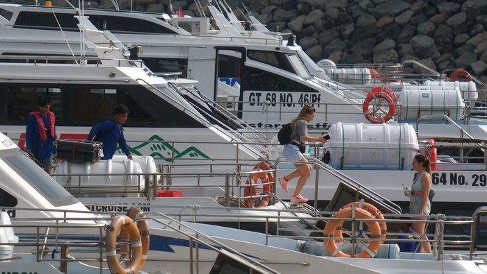 Wisatawan berjalan di dermaga apung saat akan menyeberang ke Pulau Nusa Penida menggunakan kapal cepat di Pelabuhan Sanur, Denpasar, Bali, Jumat (19/12/2025). Kantor Kesyahbandaran dan Otoritas Pelabuhan (KSOP) Kelas II Benoa, Bali, memastikan kelaikan 67 kapal cepat atau boat di Pelabuhan Sanur dan Serangan Denpasar untuk melayani peningkatan penumpang pariwisata jelang libur Natal dan Tahun Baru 2026. ANTARA FOTO/Nyoman Hendra Wibowo