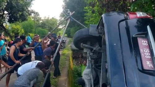 Warga berupaya mengevakuasi mobil Kantor Kemenag Lembata yang terguling, Jumat (19/12/2025).