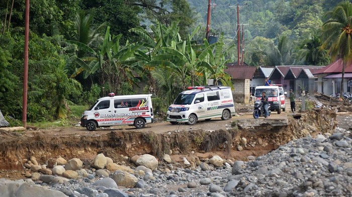 Petugas mendorong mobil ambulan saat melewati jalan darurat di Batu Busuk, Padang, Sumatera Barat, Jumat (19/12/2025). Jalan darurat tersebut kembali dibuka untuk sepeda motor dan mobil setelah beberapa waktu lalu diterjang banjir susulan sehingga membuat akses ke lokasi terdampak banjir bandang itu putus dan sempat terisolasi.  ANTARA FOTO/Iggoy el Fitra/nym.
