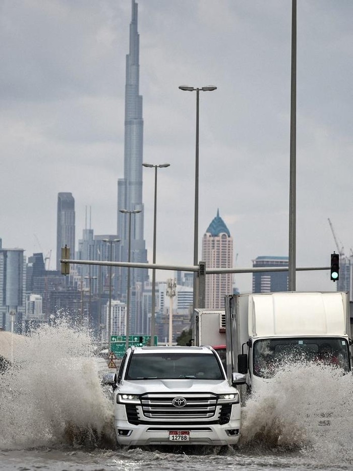 A vehicle drives through flood waters with Burj Khalifa in the background, following heavy rains, in Dubai on December 19, 2025. Dubai police urged residents on December 18, 2025, to stay indoors unless it was 