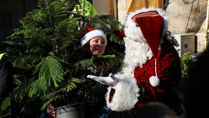 A woman selects a tree next to a person dressed as Santa Claus during an annual distribution of Christmas trees to residents by Jerusalem's municipality, in Jerusalem's Old City, December 18, 2025. REUTERS/Ronen Zvulun
