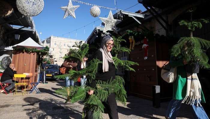 A woman selects a tree next to a person dressed as Santa Claus during an annual distribution of Christmas trees to residents by Jerusalem's municipality, in Jerusalem's Old City, December 18, 2025. REUTERS/Ronen Zvulun