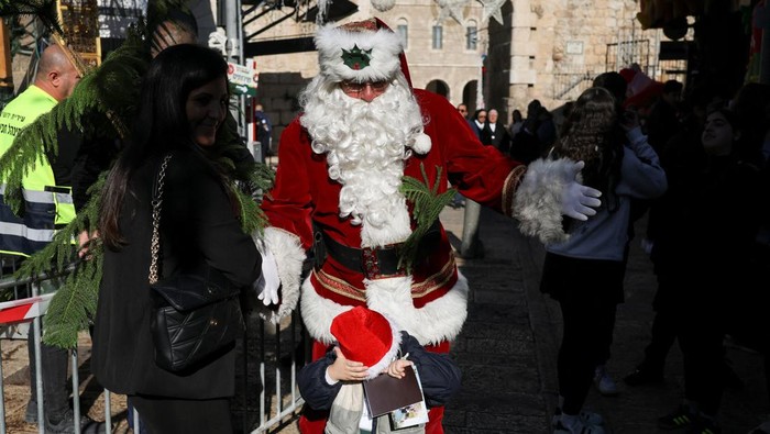 A woman selects a tree next to a person dressed as Santa Claus during an annual distribution of Christmas trees to residents by Jerusalem's municipality, in Jerusalem's Old City, December 18, 2025. REUTERS/Ronen Zvulun