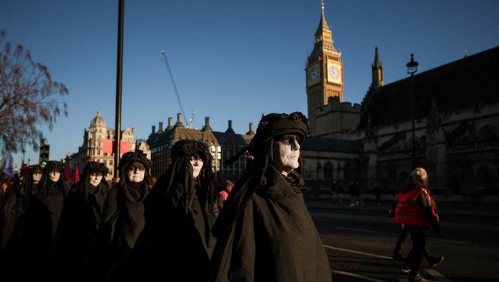 Extinction Rebellion 'Oil Slicks' performance group members stage a protest near the Elizabeth Tower, commonly referred to as Big Ben, as the group says political leaders have failed to meet climate commitments and marking the passing of the 1.5 C Paris climate goal, in London, Britain, December 20, 2025. REUTERS/Isabel Infantes      TPX IMAGES OF THE DAY