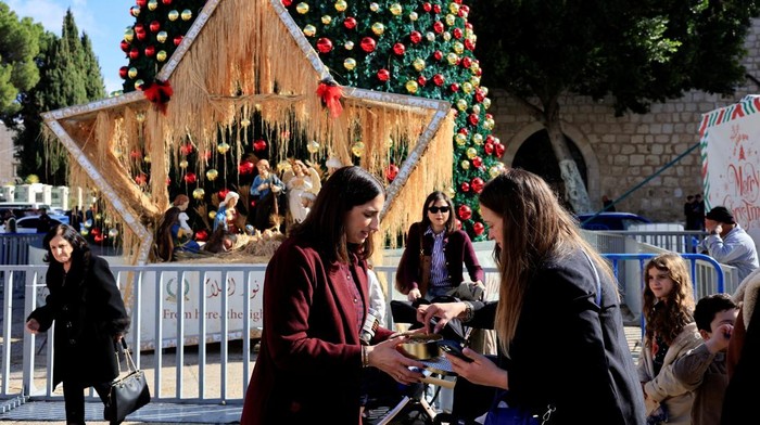 Palestinian Maria Khoury gives samples of her chocolates in a Christmas market, in the Manger Square, near the Church of the Nativity in Bethlehem in the Israeli-occupied West Bank, December 14, 2025. REUTERS/Mussa Qawasma