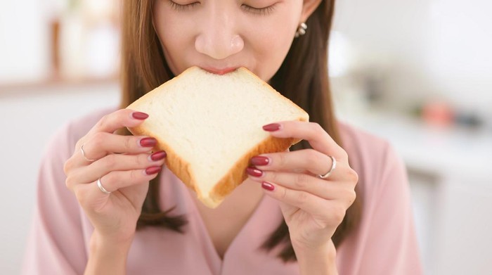 Closeup asian woman eat white toast at home - unhealthy food concept