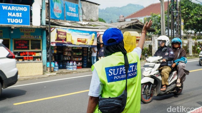 Sejumlah Supeltas mengenakan rompi hijau neon dan topi biru bersiaga di salah satu titik rawan macet Jalur Puncak, Bogor, Rabu (24/12/2025).