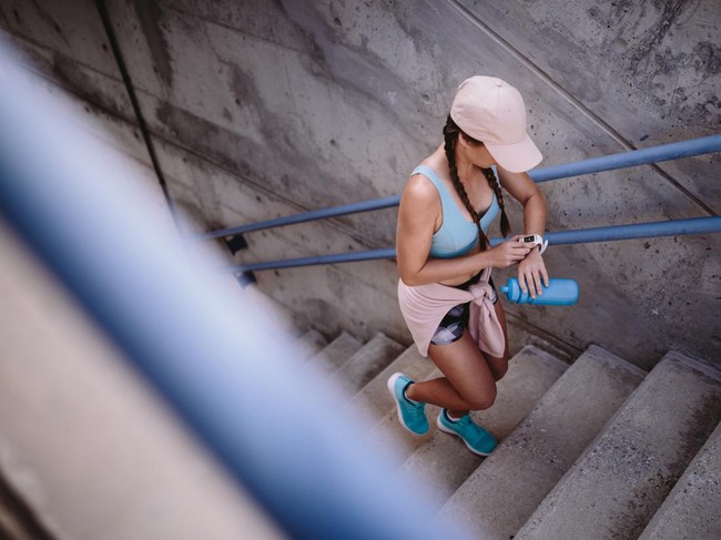 Sporty woman working out by running up urban stairs and monitoring heart rate on smartwatch