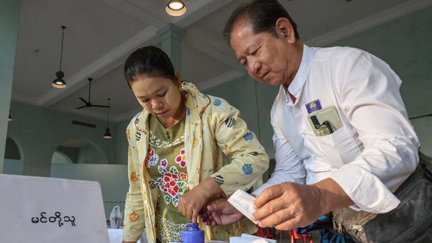 Seorang petugas pemilu membantu seorang wanita saat memberikan suara di Tempat Pemungutan Suara No. 1 Kecamatan Kyauktada, pada hari pemilihan umum di Kyauktada, Myanmar, 28 Desember 2025. (REUTERS/Stringer)