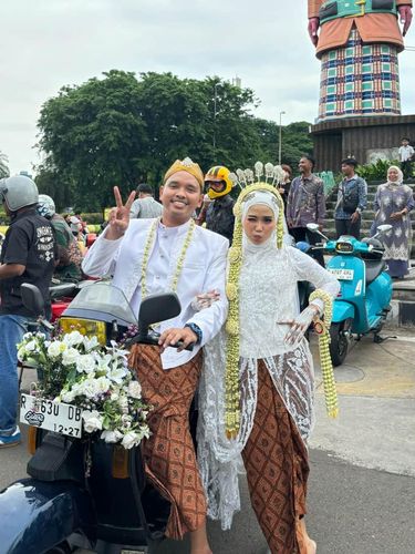Foto pernikahan Muhammad Luthfi Reza Izzulhaq dan Leny Cleriyani, pasangan pengantin yang viral usai aksi iring-iringan naik Vespa. Tampil unik ala Sunmori, pasangan ini tampil anggun dikawal puluhan motor Vespa.