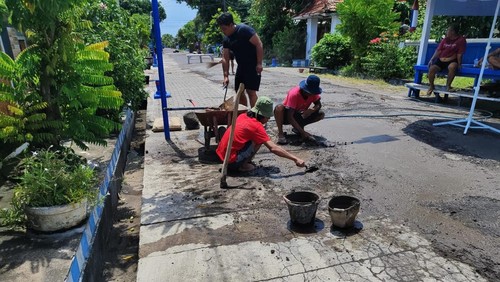 Puluhan warga saat melakukan perbaikan jalan secara swadaya di Lingkungan Asih, Kelurahan Gilimanuk, Kecamatan Melaya, Kabupaten Jembrana, Minggu (28/12/2025).